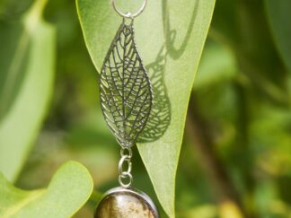 Handgefertigter zweiteiliger Anhänger aus Edelstahl mit einem stilisierten Blatt-Charm und einem 12 mm großen Glascabochon, hinter dem ein feines Blattskelett eingefasst ist – Gesamtlänge ca. 50 mm.