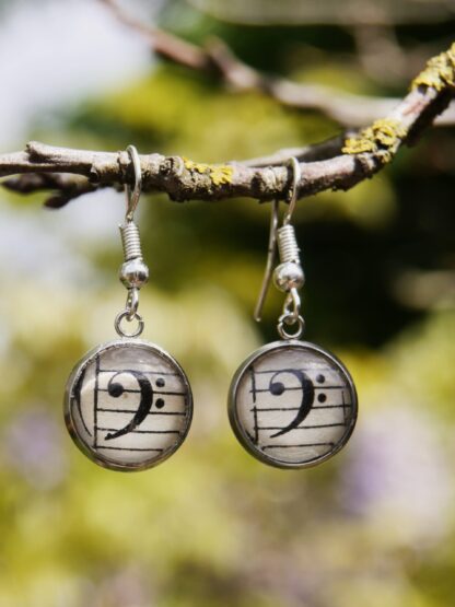Edelstahl-Ohrringe mit Haken und 12 mm Glascabochons, hinter denen ein Bassschlüssel auf antikem Notenpapier eingefasst ist – handgefertigter musikalischer Schmuck.