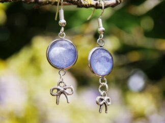 Ohrringe mit Edelstahlhaken, 12 mm Glascabochons mit eingefasster blau-grauer Hortensienblüte und dekorativem Schleifencharm – handgefertigter Naturschmuck.