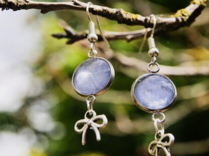 Ohrringe mit Edelstahlhaken, 12 mm Glascabochons mit eingefasster blau-grauer Hortensienblüte und dekorativem Schleifencharm – handgefertigter Naturschmuck.